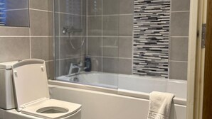 A modern bathroom with a toilet, shower, and bathtub. - Cosy City Centre Apartment with parking (West Midlands)