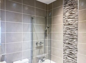 A modern bathroom with a glass-enclosed shower, a toilet, and a decorative wall panel.