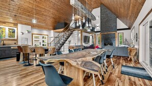 Amplia sala de estar con una gran mesa de comedor de madera, sillas modernas y una escalera que lleva a un nivel superior.