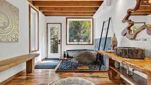 Un interior rústico con chimenea de piedra, vigas de madera y un ventanal con vistas a árboles.