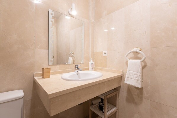 Un baño con lavamanos de mármol color crema, un espejo y un perchero para toallas.