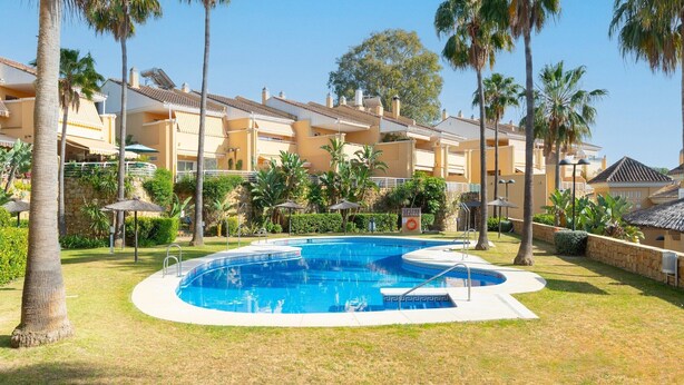 A swimming pool surrounded by palm trees and a building with balconies.