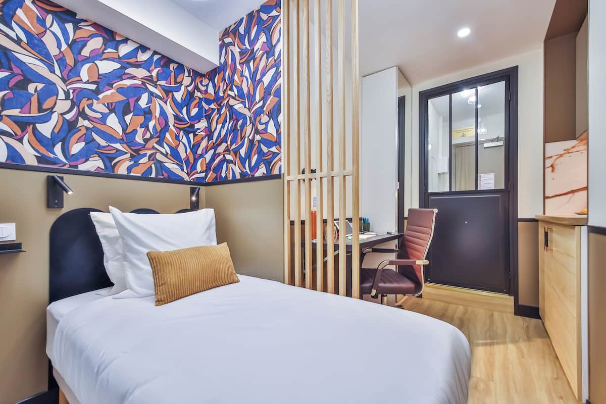 A hotel room with a bed, a desk, a chair, and a large abstract mural on the wall.