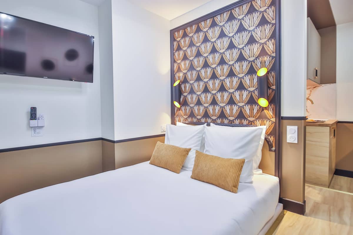 A hotel room with a bed, a TV mounted on the wall, and a patterned headboard.
