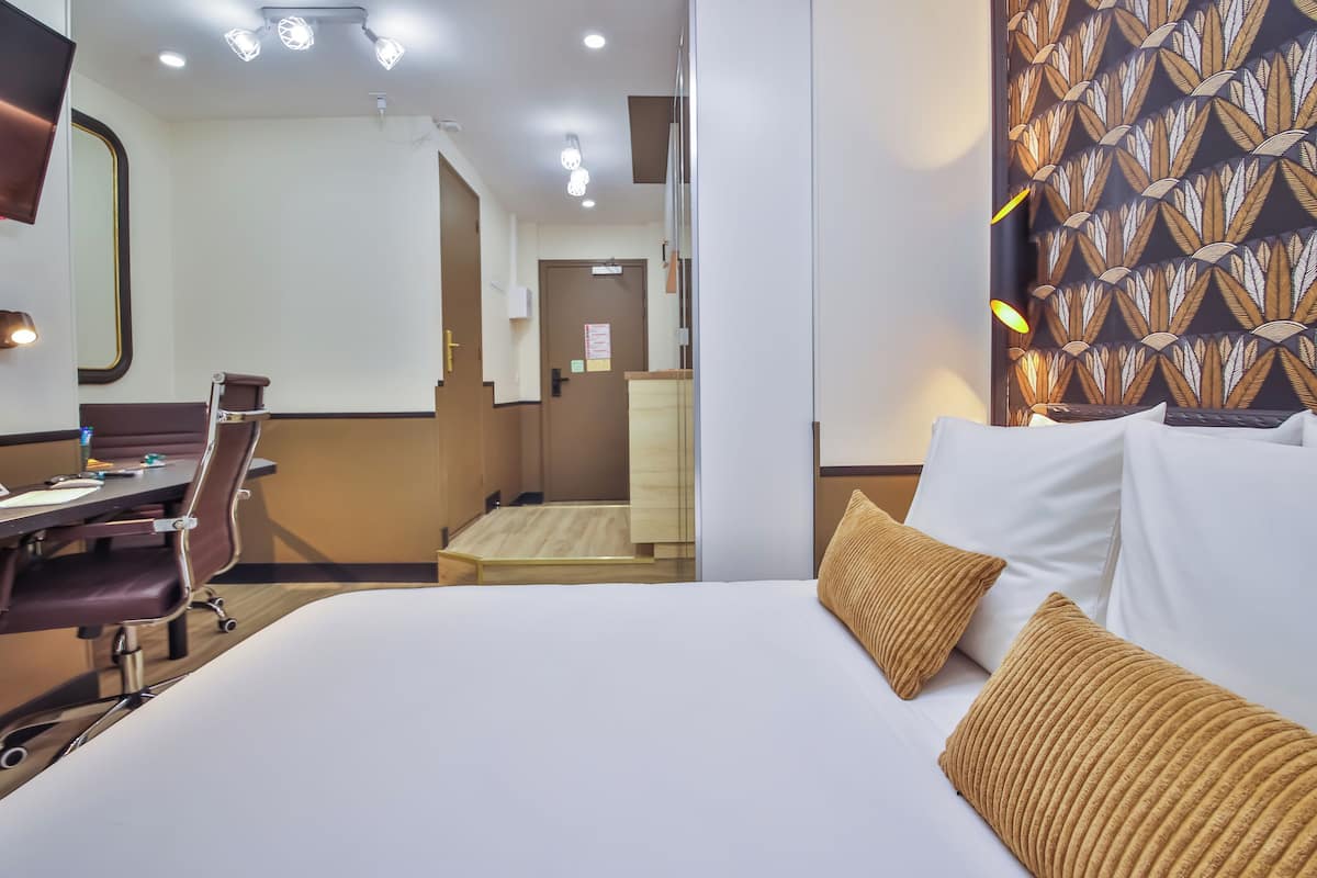 A hotel room with a bed, a desk, and a chair. There is a mirror on the wall and a door leading to another room.