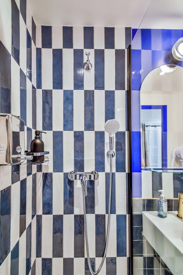 A bathroom with a checkered tile wall, a handheld showerhead, and a glass-enclosed sink area. - WS - Opéra - Malesherbes (Paris)