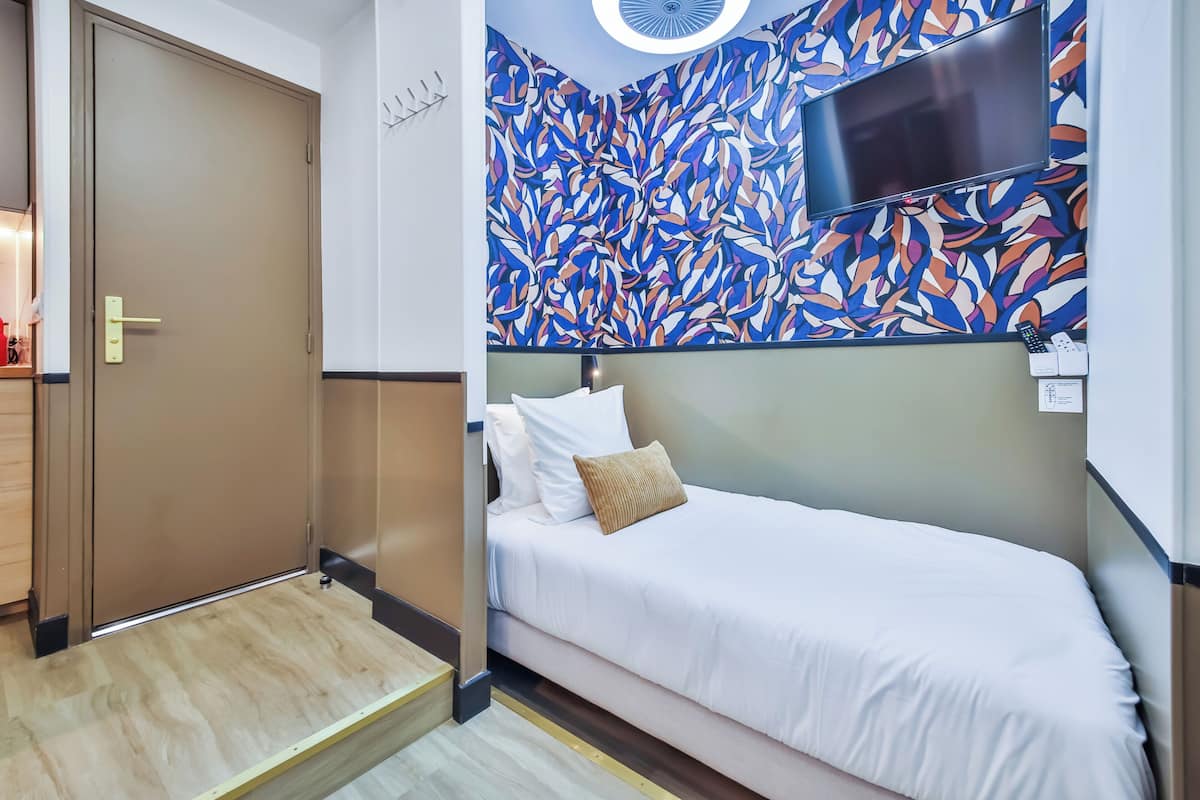 A hotel room with a bed, a TV mounted on the wall, and a door.
