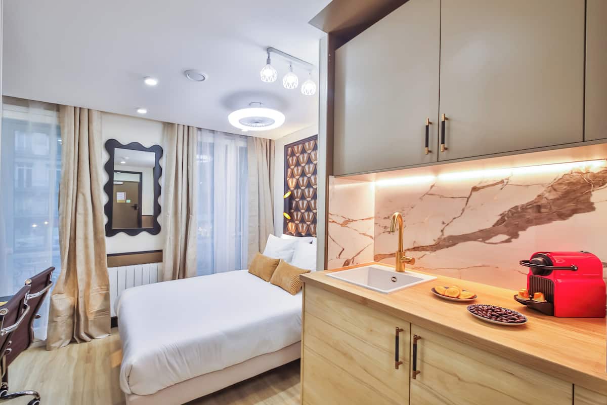 A modern hotel room with a bed, a vanity with a mirror, a sink, and a red coffee machine.