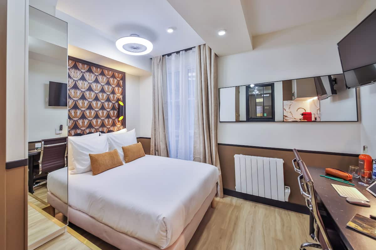 A hotel room with a large bed, a desk with a computer, a mirror, and a TV.