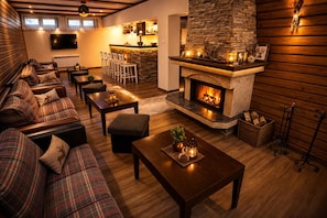 A cozy living room with a fireplace, a sofa set, a dining area, and a kitchen in the background.