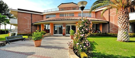 Un edificio de dos pisos con una entrada curva, un camino pavimentado y plantas en macetas.