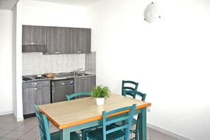 Une cuisine compacte avec des meubles gris, un évier en acier inoxydable et une petite table à manger avec deux chaises.