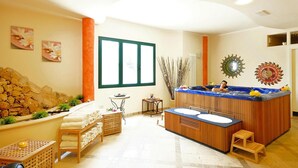 A spa room with a wooden bathtub, a small table with a candle, and a stone wall. - Villa in Cecina Mare Near Sandy Beaches (Cecina)