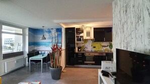 A modern kitchen with dark cabinets, a microwave, and a sink. There is a dining area with a table and chairs, and a large window with a view of the sea. - Welcome to apartment 20 in house 1 of the Vier Jahreszeiten complex (Großenbrode)