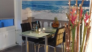 A dining area with a view of the ocean, a hanging pendant light, and a potted plant with tall stems. - Welcome to apartment 20 in house 1 of the Vier Jahreszeiten complex (Großenbrode)