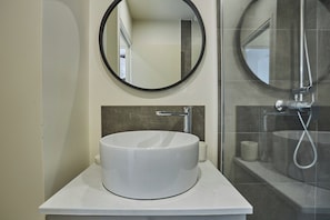 A bathroom with a white sink, a round mirror, and a shower area.