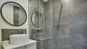 Een moderne badkamer met een ronde spiegel, een witte wastafel en een douchecabine met glazen wanden.