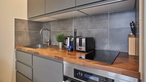 Een moderne keuken met grijze tegels, roestvrijstalen apparatuur en houten aanrechtbladen.