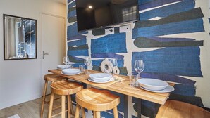 Een eetgedeelte met een houten tafel voor vier personen, een wandgemonteerde flatscreen televisie en een behang met patroon achter de tafel.