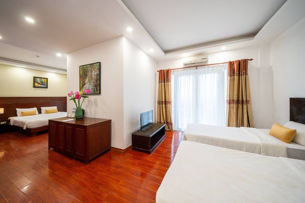 A hotel room with two beds, a wooden floor, a TV, and a painting on the wall.
