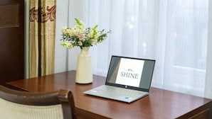 A laptop on a wooden table with a vase of flowers and a curtain in the background. - Shine Hue Hotel 2  (Hue)