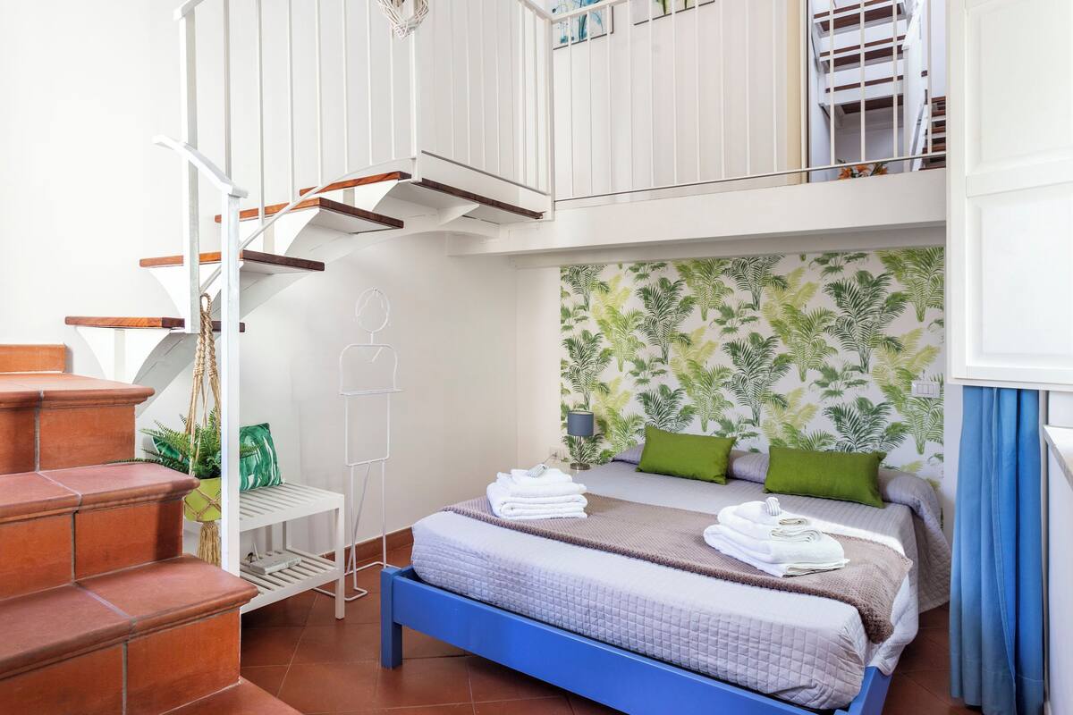 A bedroom with a bed, a staircase, and a balcony.