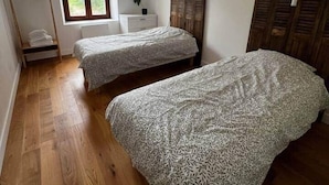 A bedroom with two beds, a window, a wooden floor, and a ceiling light fixture.