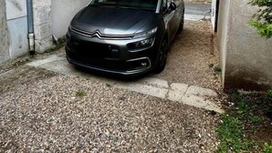 A black car parked under a covered area with a gravel driveway.