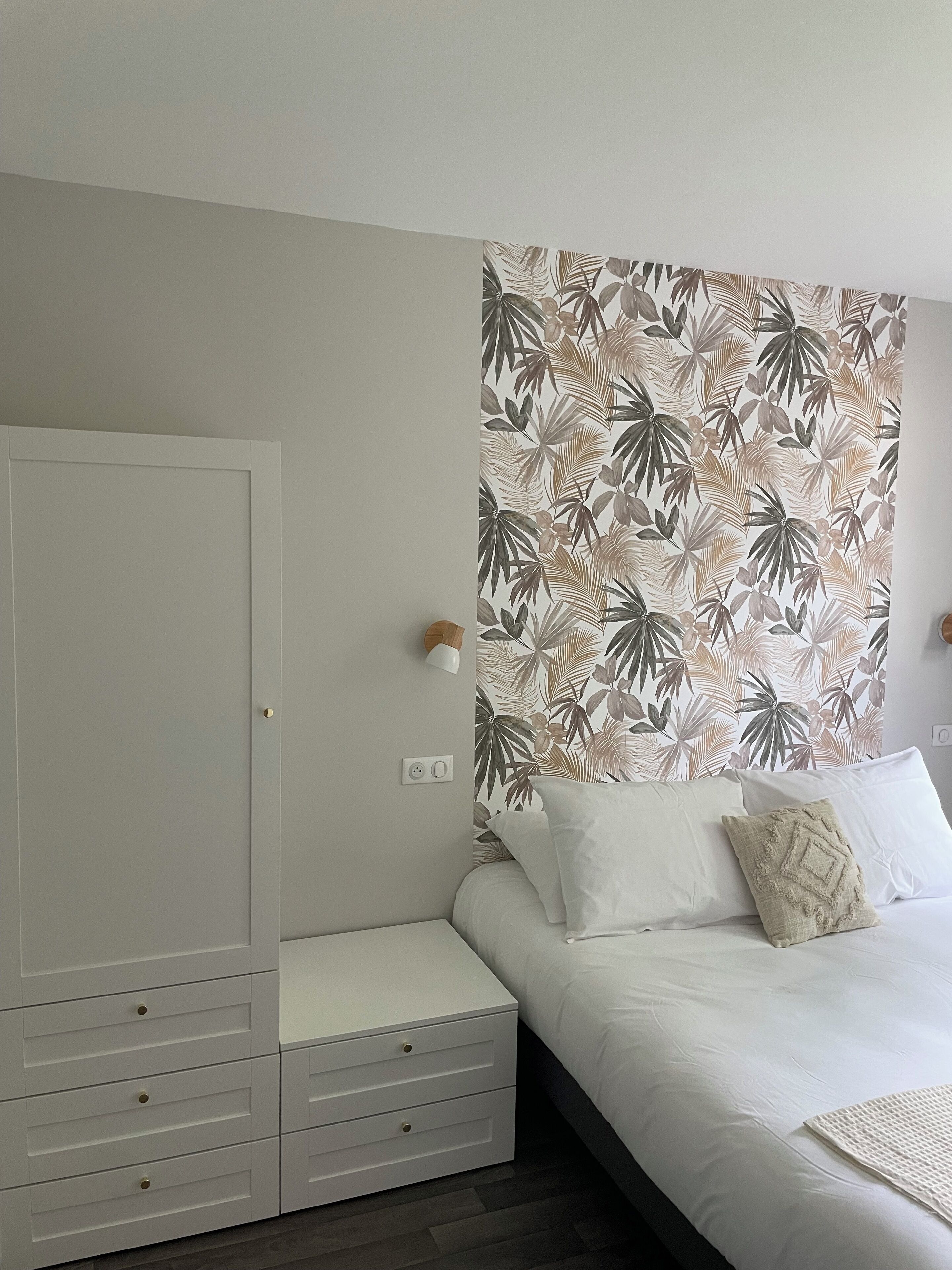 A bedroom with a bed, a wardrobe, a wall-mounted light, and a power outlet.
