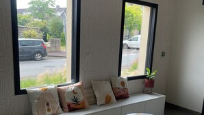 A modern room with a white bench along a window, two small round tables, and a potted plant. - Ducey Appart'hôtel  (Ducey-les-Chéris)