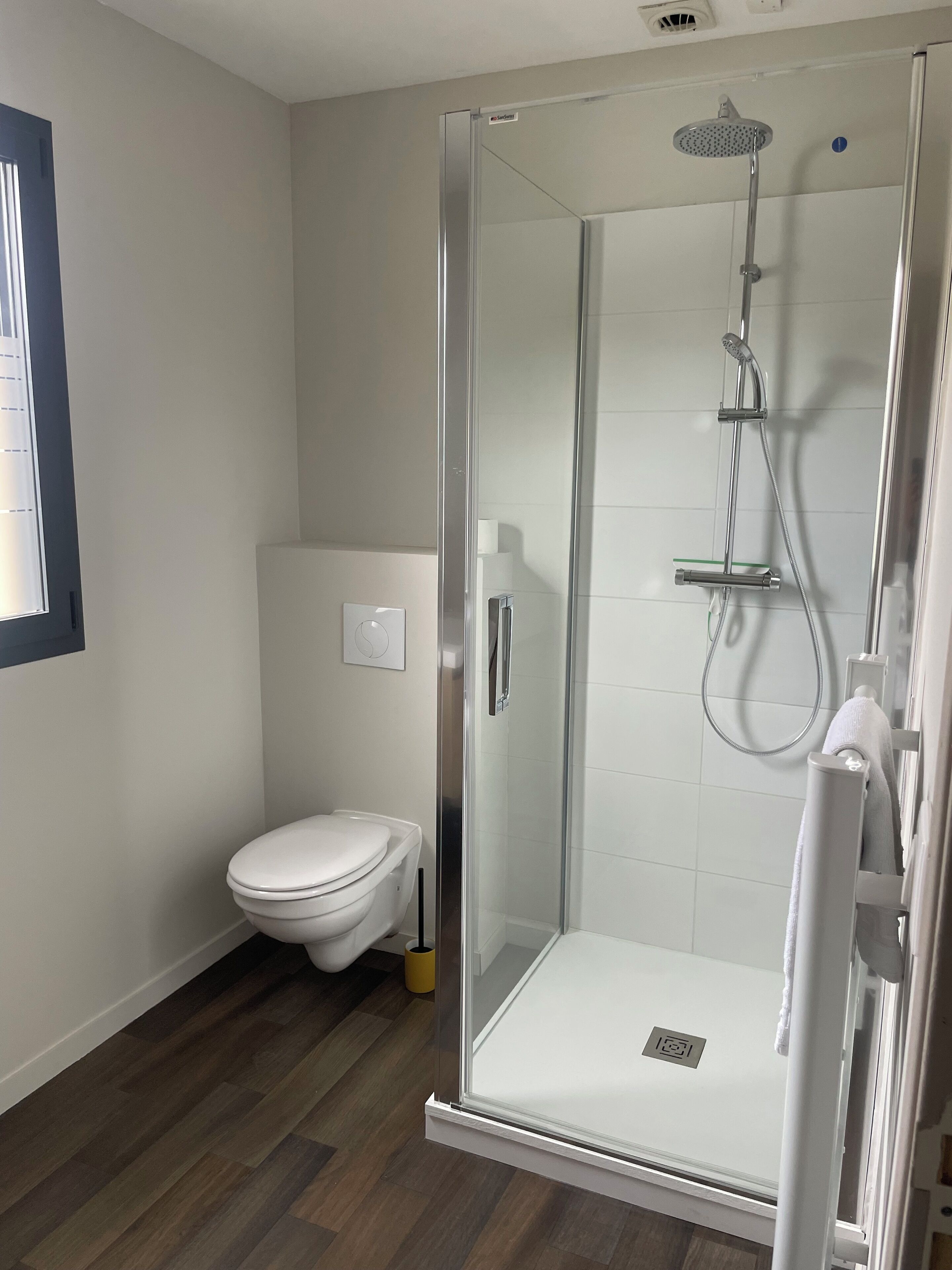 Une salle de bain moderne avec une douche à parois de verre, des toilettes et un plancher en bois.