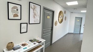 A hallway with framed artwork, a white console table with brochures, and a door with a sign. - Ducey Appart'hôtel  (Ducey-les-Chéris)