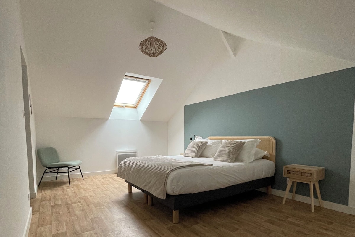 A bedroom with a bed, a chair, a small table, and a skylight.