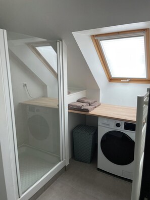 A compact laundry room with a washing machine, a dryer, and a small trash bin. - Ducey Appart'hôtel (Ducey-les-Chéris)