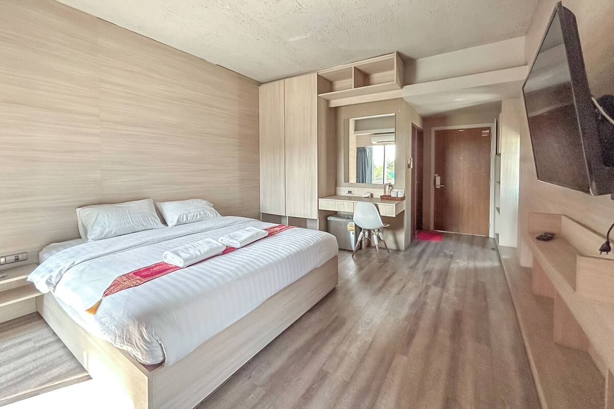 A hotel room with a large bed, a desk, a chair, and a TV.