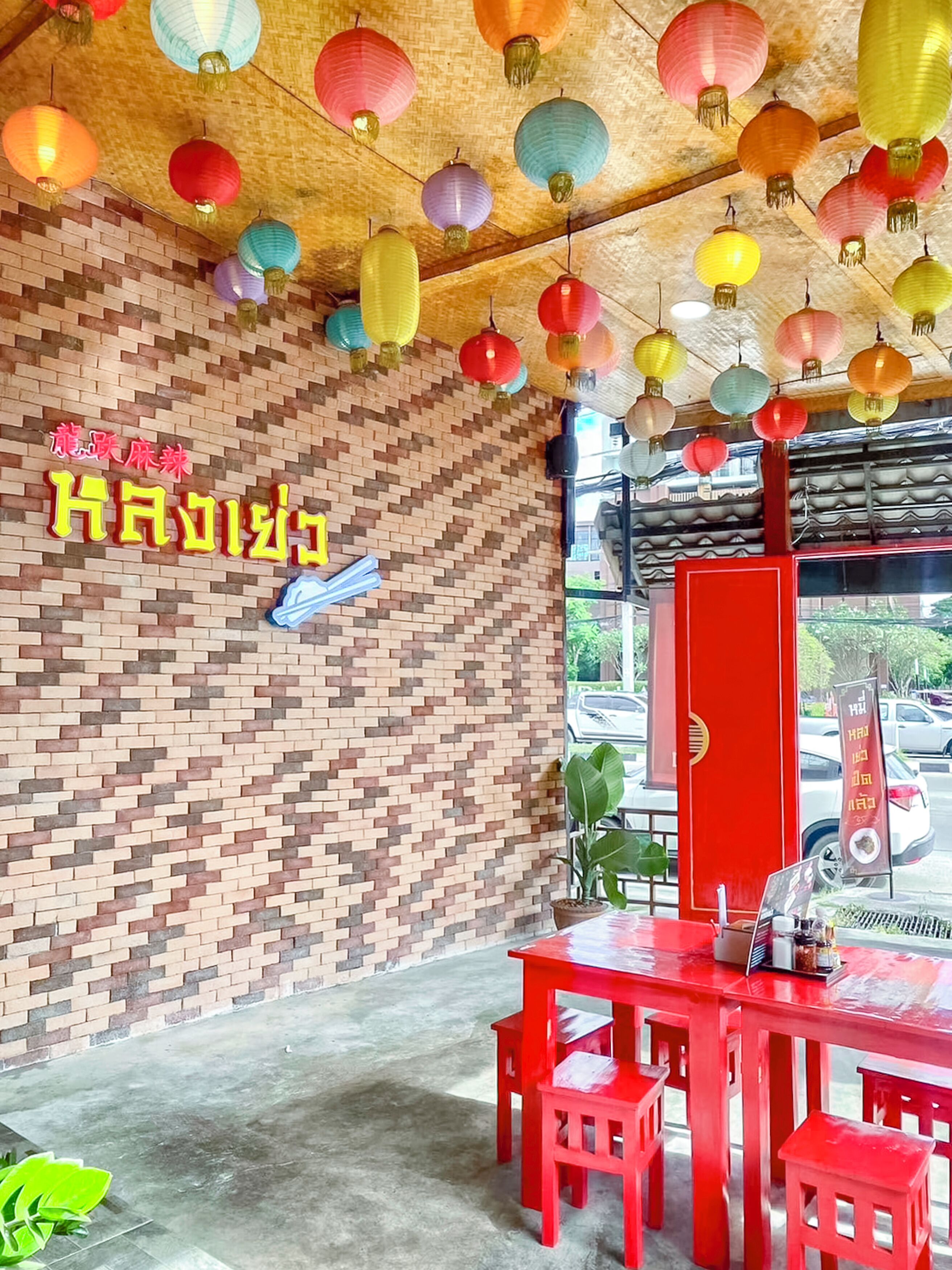 L’intérieur d’un restaurant avec un mur en briques, des lanternes colorées suspendues, une table rouge avec des chaises et une enseigne avec des caractères chinois.