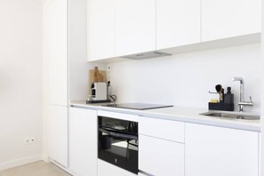 A modern kitchen with white cabinetry, a built-in oven, a countertop with a coffee machine, and a sink with a faucet.