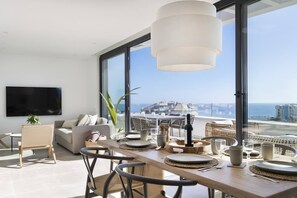 A modern living room with a dining area, large windows, and a view of the city.