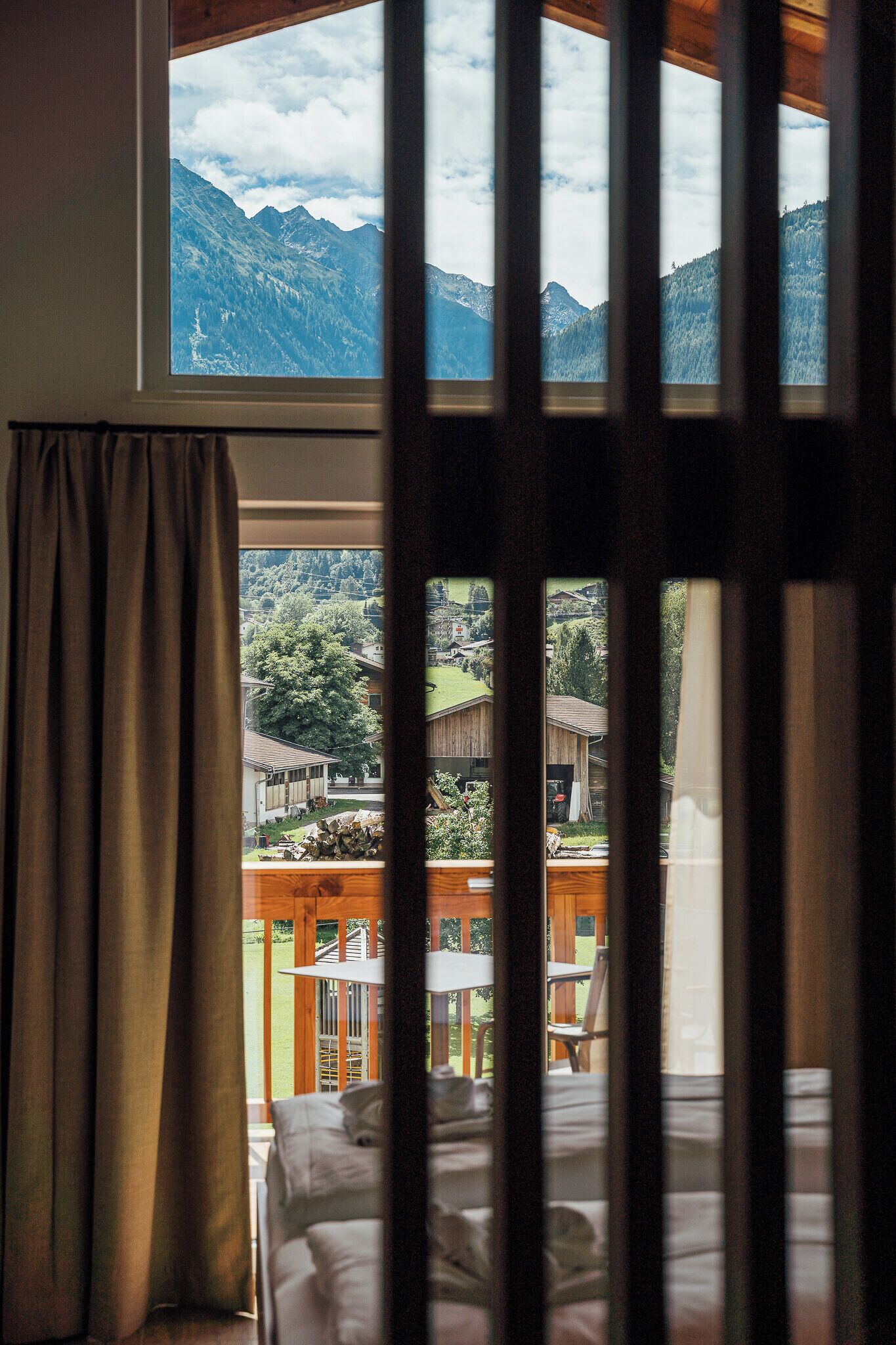 A bedroom with a large window overlooking a mountainous landscape and a village below.