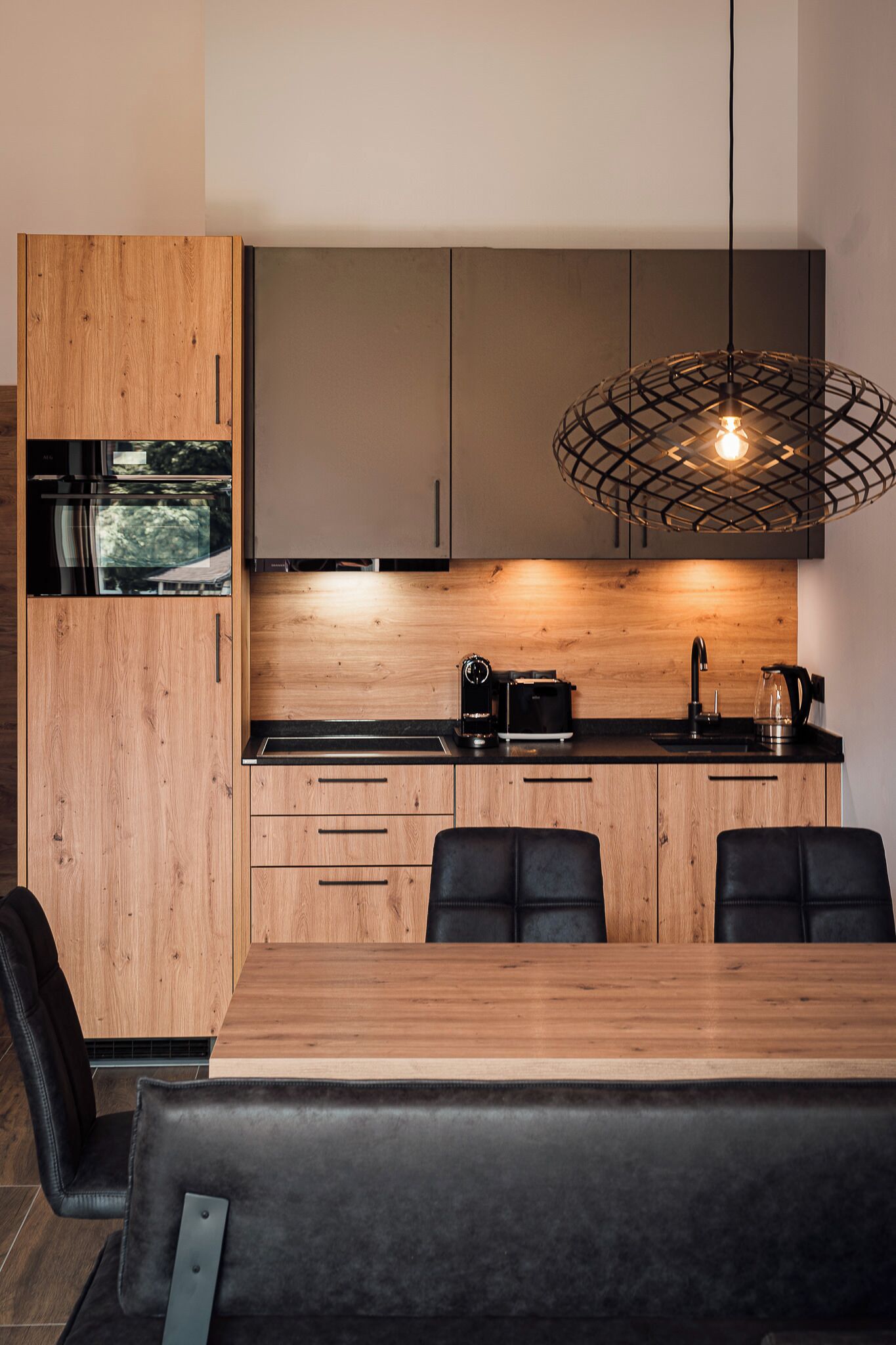 A modern kitchen with wooden cabinets, a black countertop, and a dining area with a wooden table and black chairs.