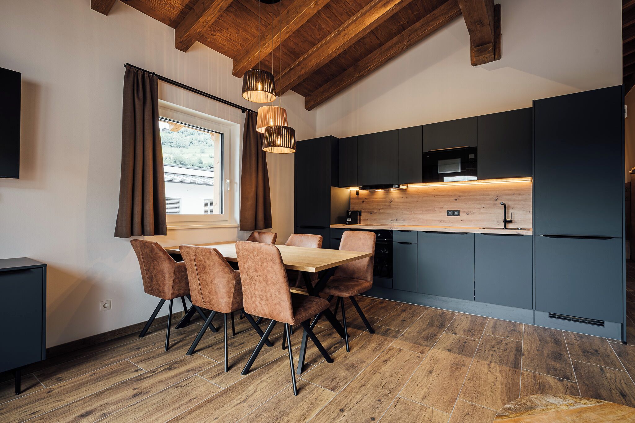 A modern kitchen with dark cabinets, a wooden dining table, and six chairs.