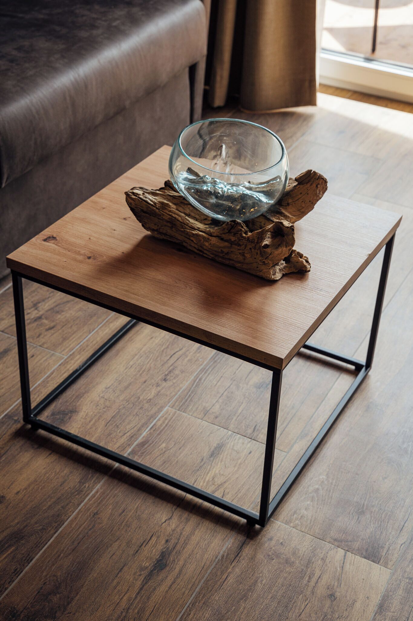 A square wooden table with metal legs, a glass bowl, and a piece of driftwood on top.