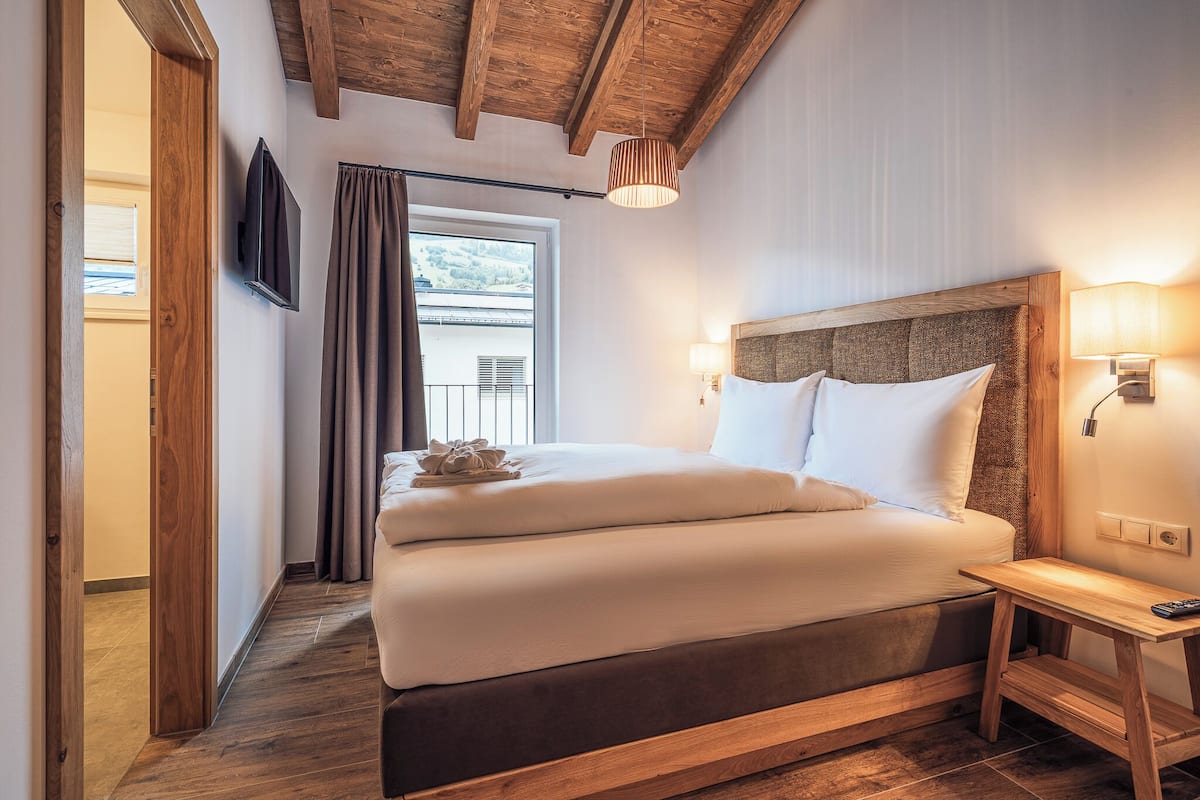 Un dormitorio con cabecera de madera, una mesita de noche con lámpara y una ventana con cortinas.