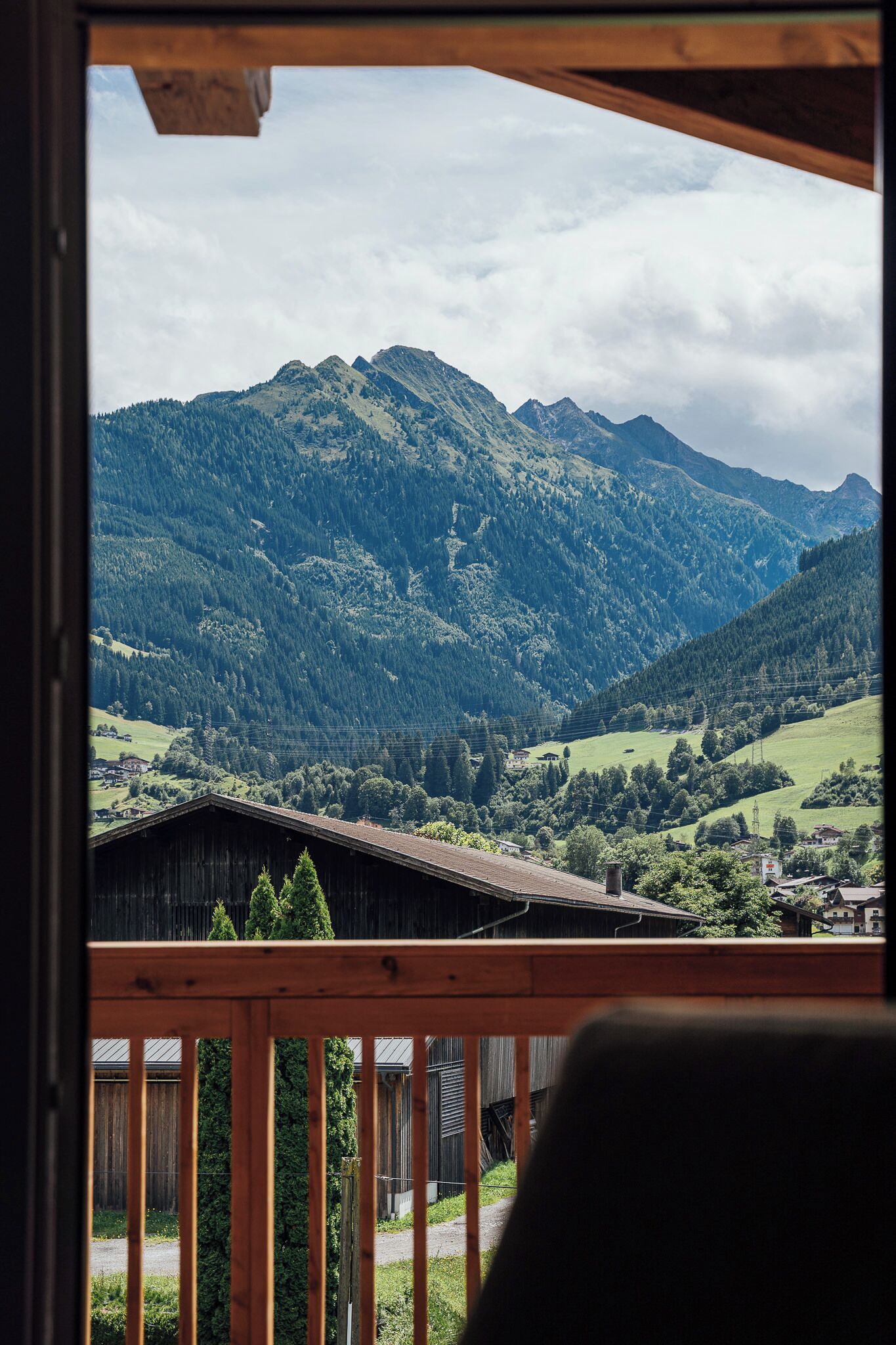 A view from a wooden balcony overlooking a mountainous landscape with a wooden cabin and a road in the foreground.