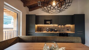A modern kitchen with dark cabinets, a wooden dining table, and a large window overlooking a balcony. - Der Kehlbachwirt by Monteviva (Niedernsill)