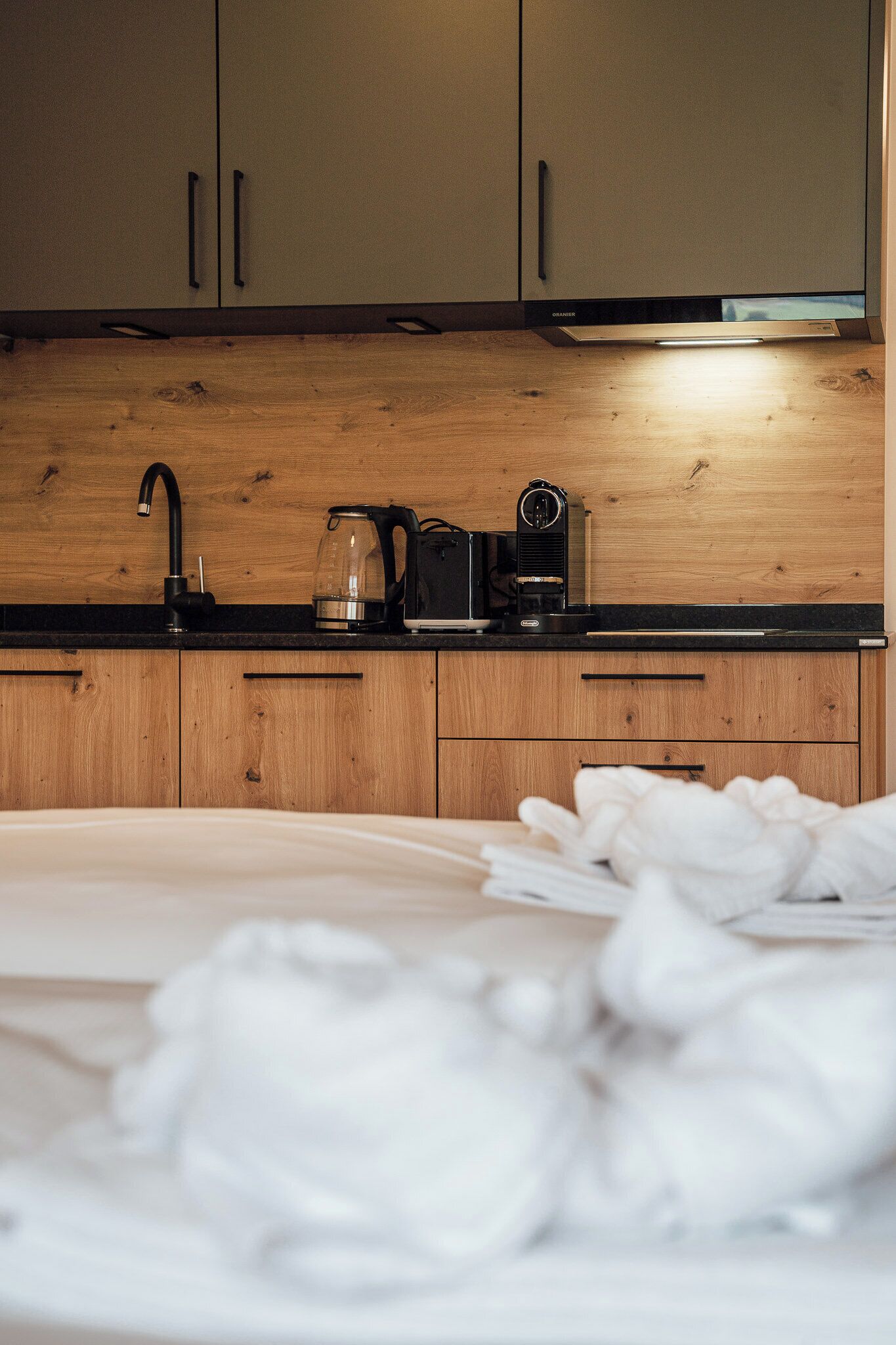 Une cuisine moderne avec des meubles en bois, un plan de travail noir, une machine à café et une bouilloire.