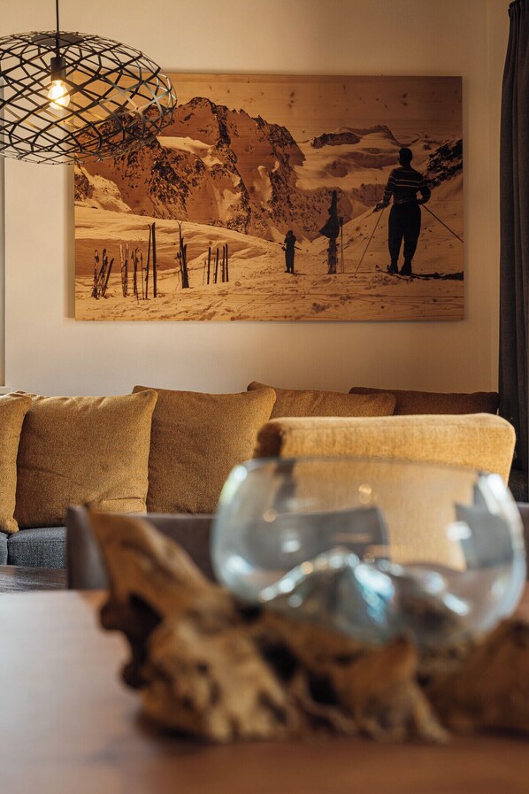 A living room with a large painting of a mountainous landscape, a wooden coffee table with a glass bowl, and a hanging light fixture. - Der Kehlbachwirt by Monteviva (Niedernsill)