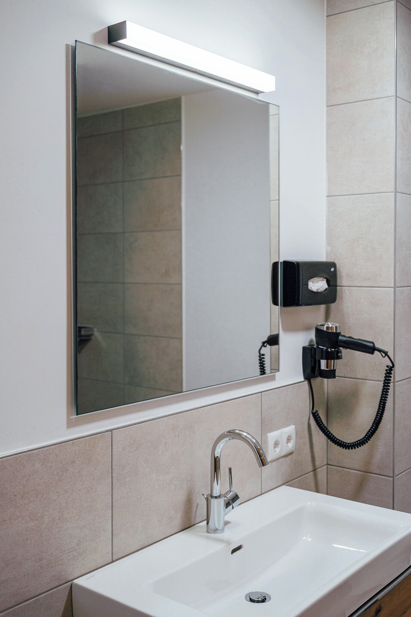 Une salle de bain avec un lavabo blanc, un miroir et un sèche-cheveux fixé au mur.