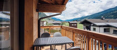 A wooden balcony with a table and chairs, overlooking a mountainous landscape.