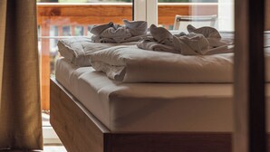 A bed with a wooden headboard, a view of a mountainous landscape through a window, and a wooden balcony railing. - Der Kehlbachwirt by Monteviva (Niedernsill)